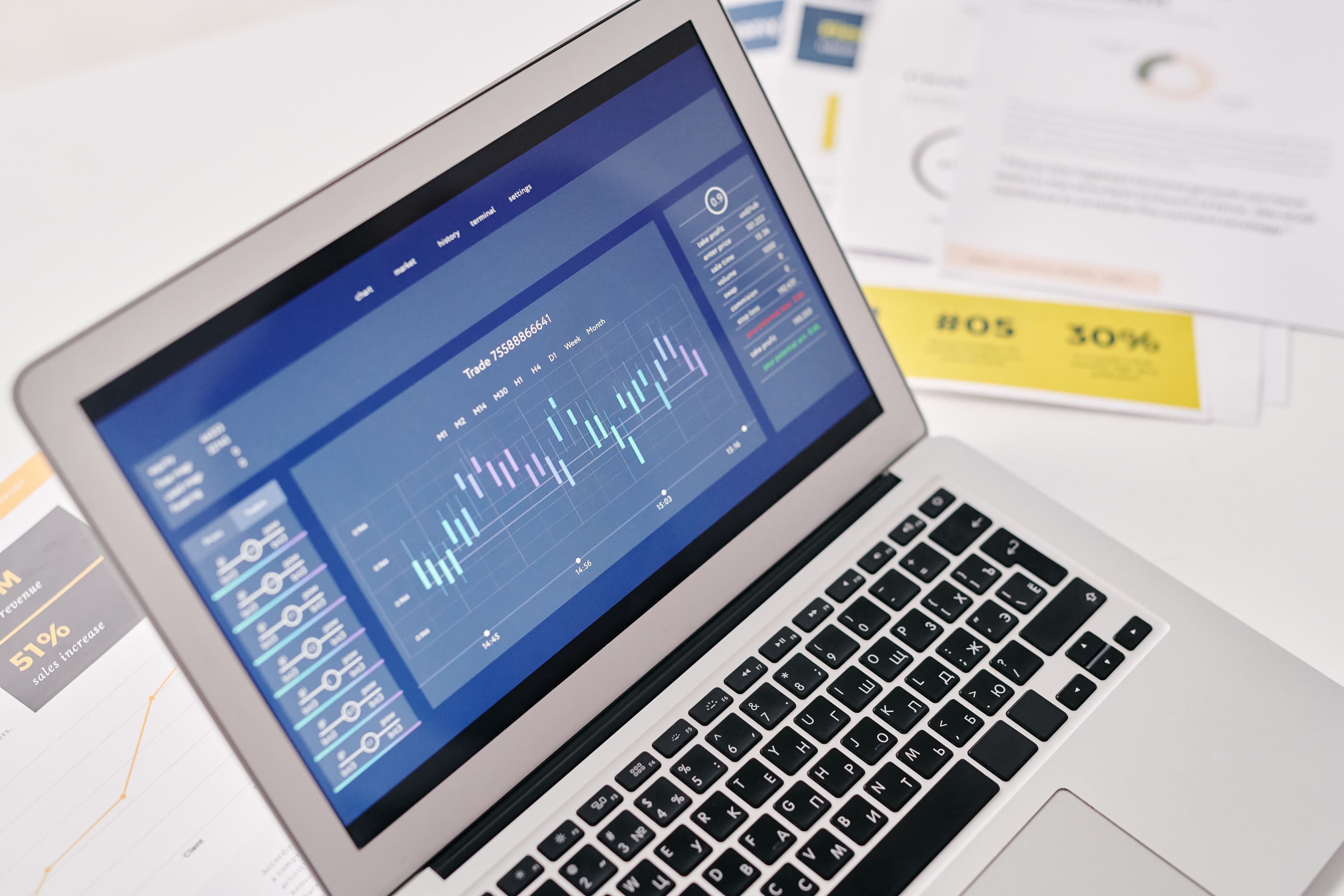 A laptop displaying detailed reports beside printed business documents