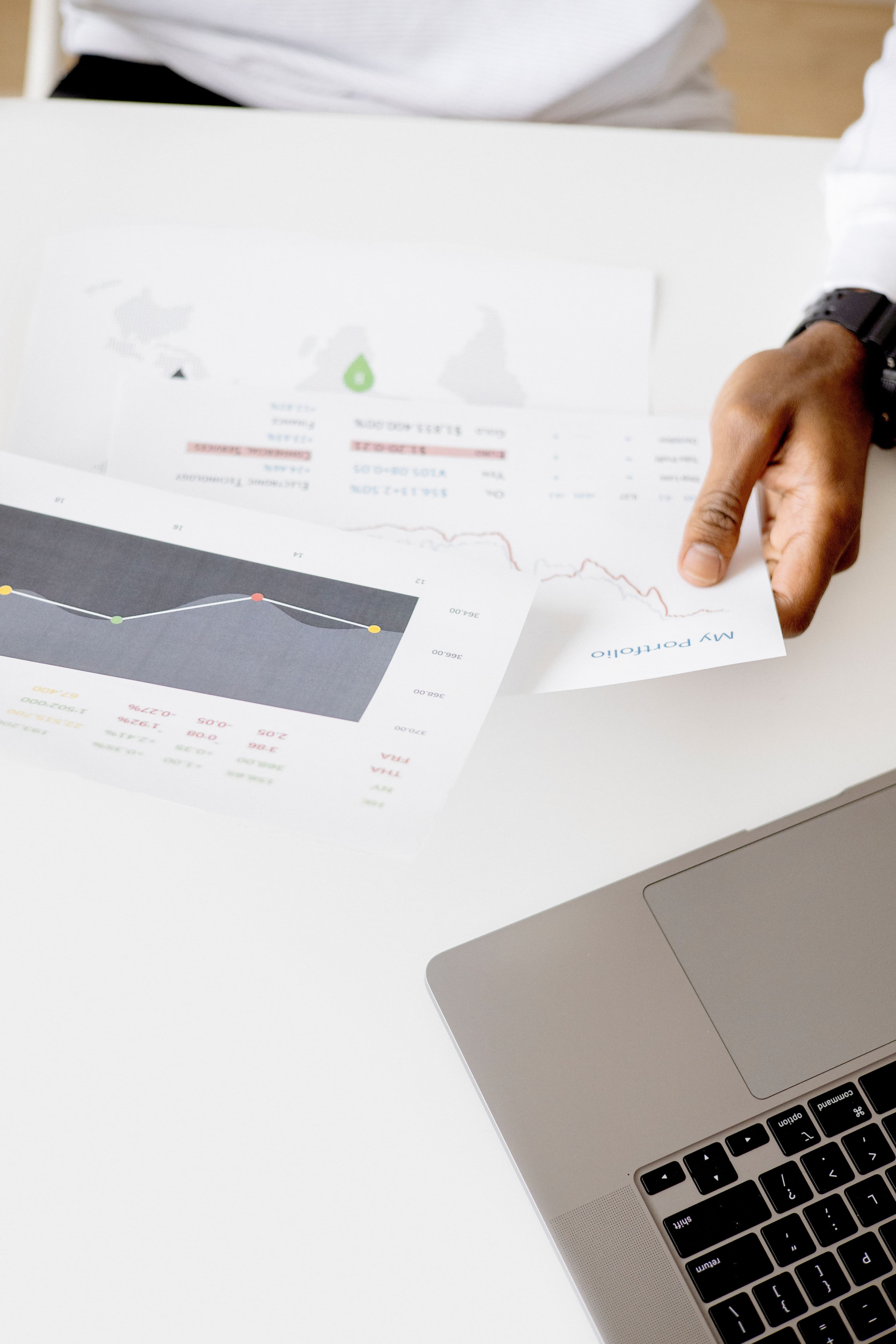 A person using a laptop to analyze printed business charts and reports